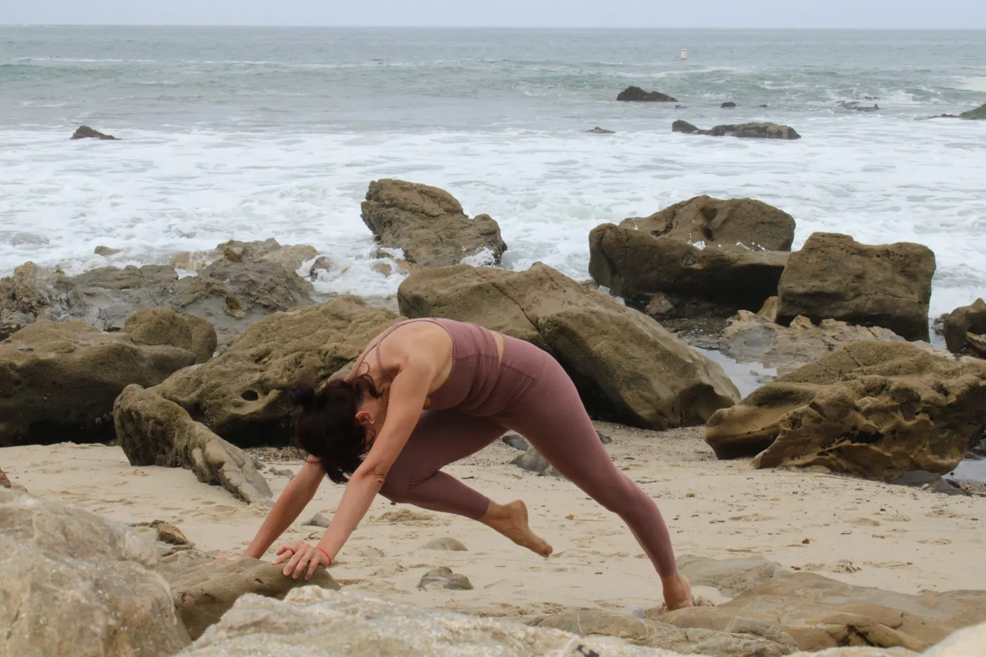 Arpi in a deep lunge stretch on the rocks in Corona Del Mar